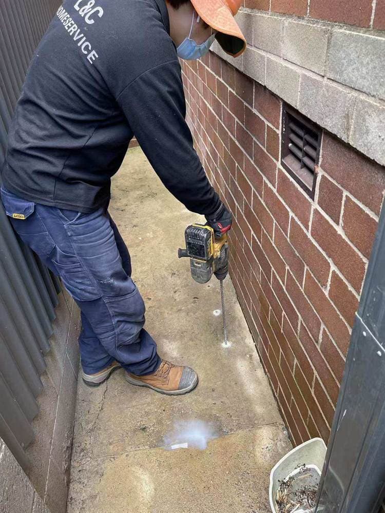Technician applying pest control treatment around a Sydney home exterior wall